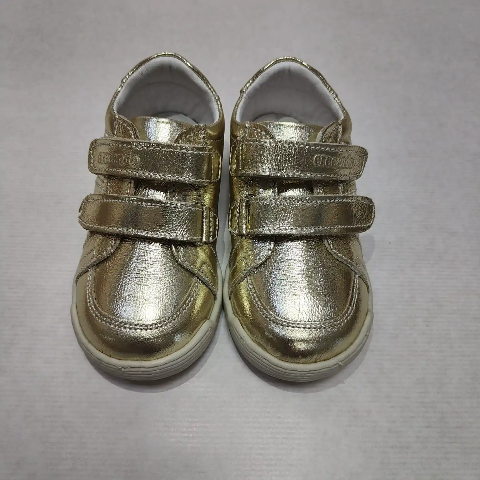 Zapato respetuoso Crescendo en piel dorada, vista frontal mostrando el diseño con doble cierre de velcro y acabados brillantes ideales para estilo y confort.